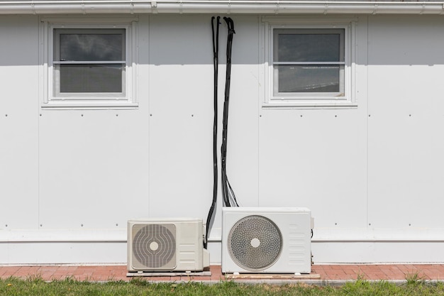 A group of outdoor air conditioner units installed on the ground in the backyard of a building