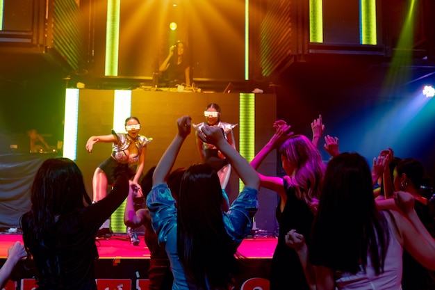 Group of people dance in disco night club to the beat of music from DJ on stage