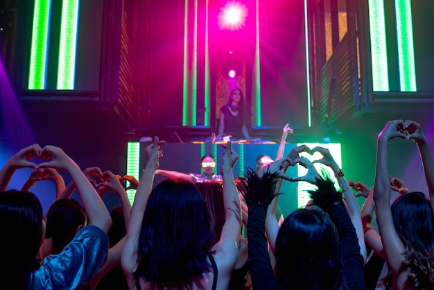 Group of people dance in disco night club to the beat of music from DJ on stage