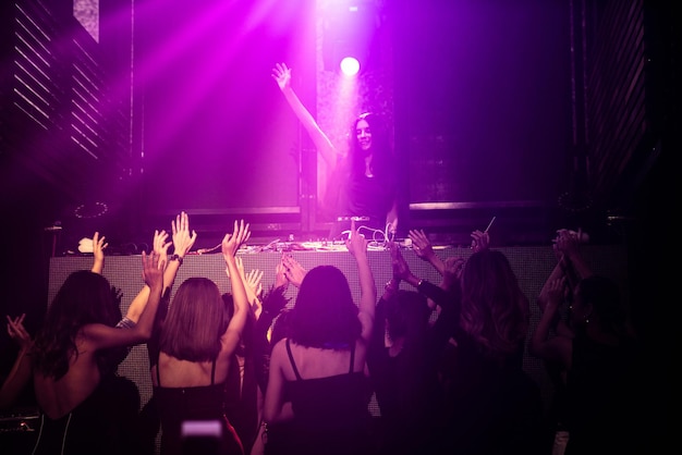 Group of people dance in disco night club to the beat of music from DJ on stage