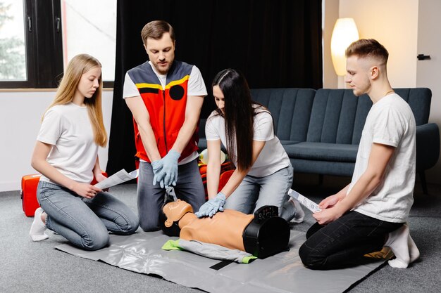 Group of people learning how to make first aid heart compressions with dummies during the training indoors