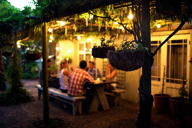 Group of people sitting outdoors at a table hanging baskets in foreground evening