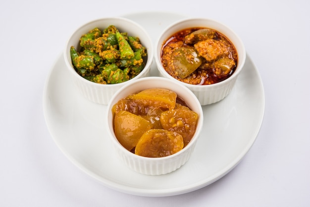 Group photograph of indian pickles like mango pickle , lemon pickle and green chilli pickle, sarved in black ceramic bowl, selective focus