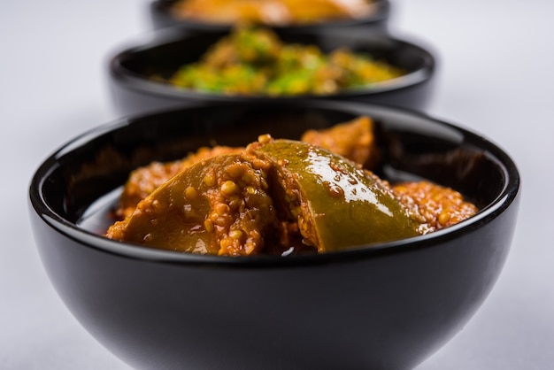 Group photograph of indian pickles like mango pickle , lemon pickle and green chilli pickle, sarved in black ceramic bowl, selective focus