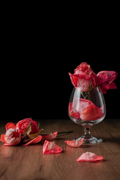 A group of pink roses put in wine glass that falling on dark color wooden table