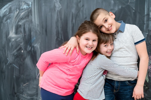 group portrait of happy kids hugging each other while having fun in front of black chalkboard