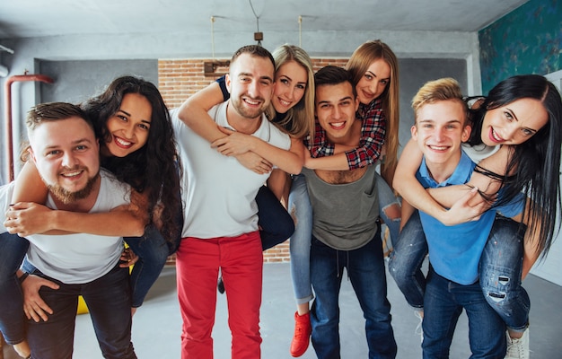 Group portrait of multi-ethnic boys and girls with colorful fashionable clothes holding friend posing on a brick wall, Urban style people having fun, s about youth togetherness lifestyle