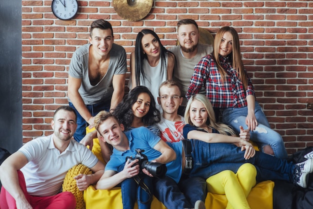 Group portrait of multi-ethnic boys and girls with colorful fashionable clothes holding friend posing on a brick wall, Urban style people having fun, s about youth togetherness lifestyle