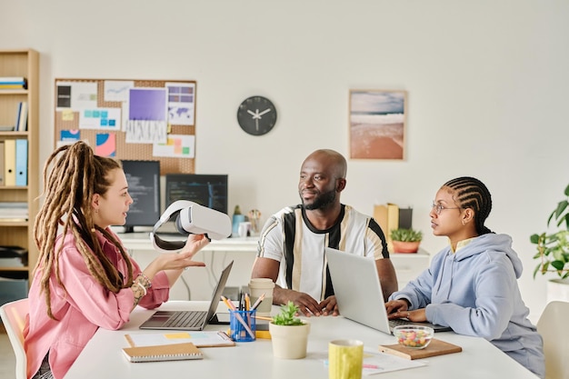 Group of programmers discussing new gadget at table in team during meeting in it office