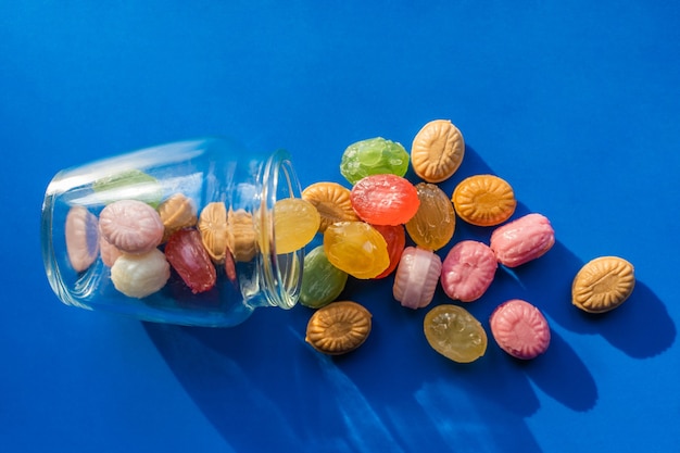 Group of Scattered Colorful candies on blue background with glass jar. Confectionery and sweets store concept. Stock photo.