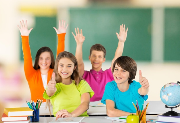 Group of school kids in classroom with hands raised