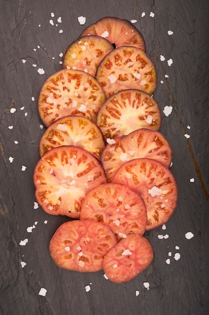 Group of sliced raf tomatoes with flake salt on green wooden background