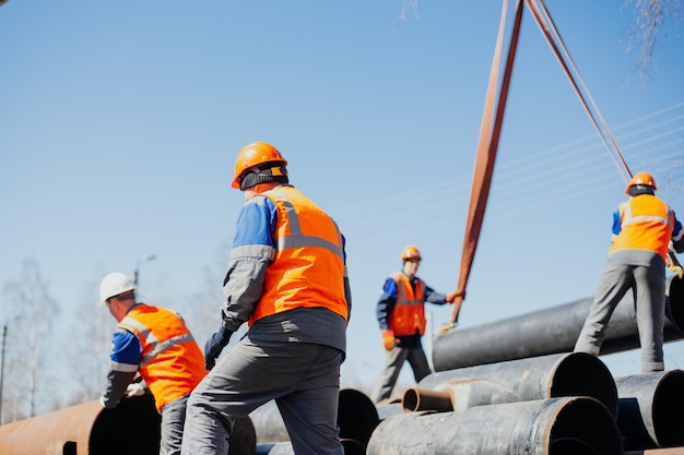 Group of slingers in construction helmets and vests on street unload metal pipes Real scene