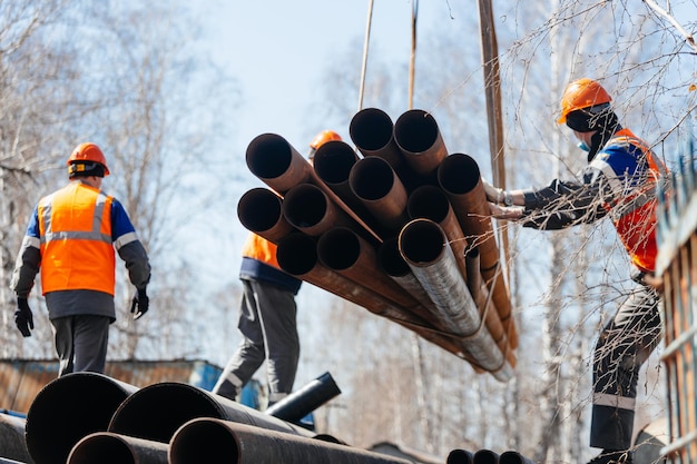 Group of slingers in construction helmets and vests on street unload metal pipes Real scene