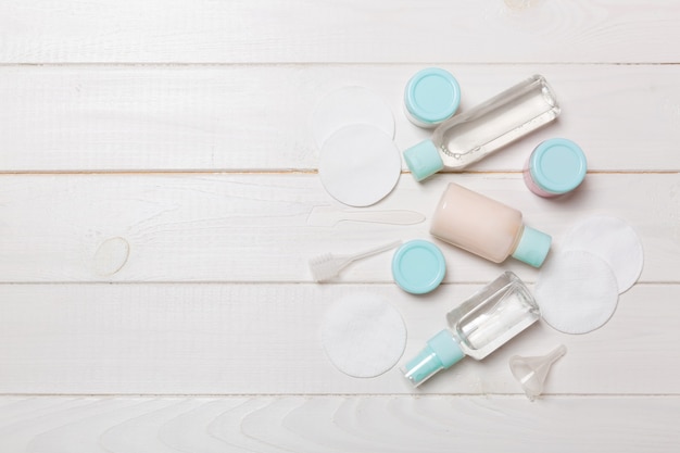 Group of small bottles for travelling on wooden background. Copy space for your ideas. Flat lay composition of cosmetic products. Top view of cream containers with cotton pads.