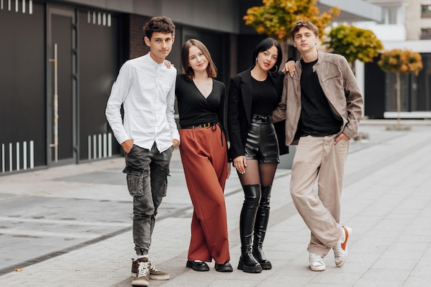 Group of smiling and happy teenage friends wearing casual clothes spending time together posing and talking with each other near college building on autumn day