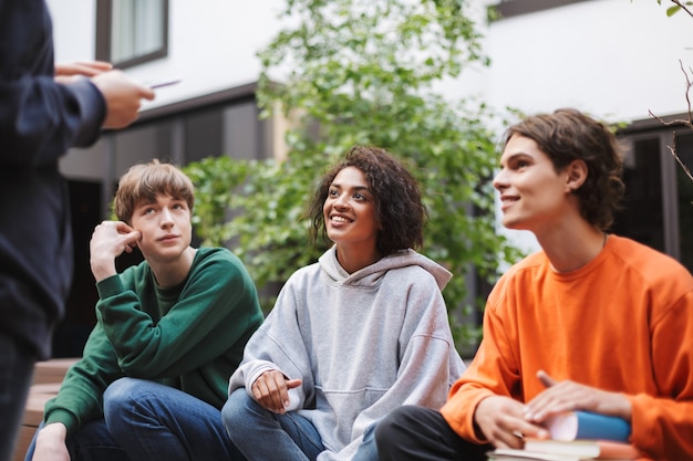 Group of smiling students sitting and dreamily looking aside while spending time together in courtyard of university