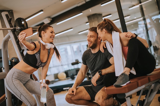 Group of sporty people in sportswear taking selfie photo with mobile phone at gym