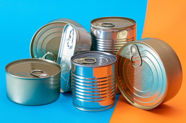 A Group of Stacked Tin Cans with Blank Edges on Split Blue and Orange Background Canned Food Different Aluminum Cans for Safe and Long Term Storage of Food Steel Sealed Food Storage Containers