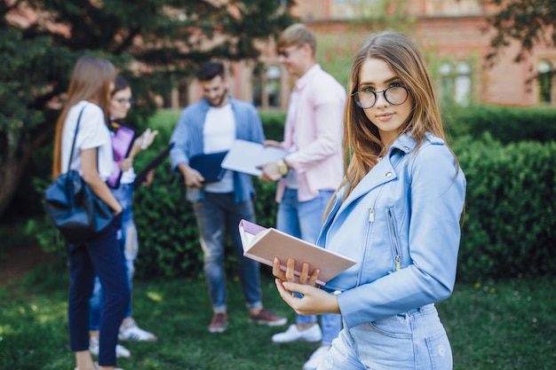 A group of students. Portrait of young girl standing on campus. Hold folder and backpack in her hands.