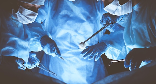 Group of surgeons wearing safety masks performing operation. Medicine concept.