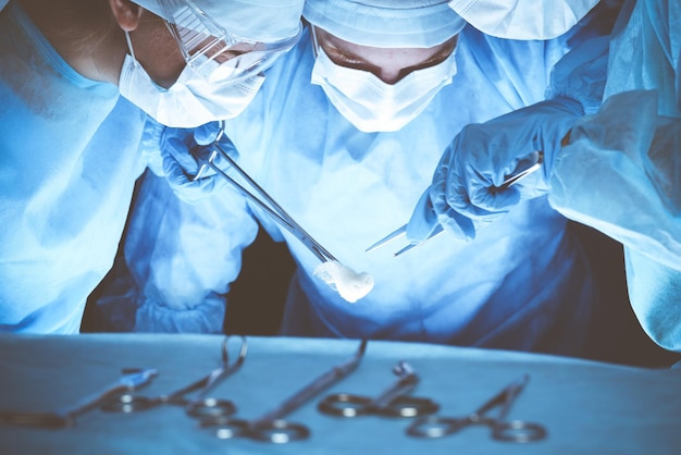 Group of surgeons wearing safety masks performing operation. Medicine concept.