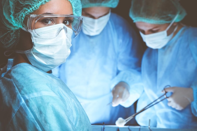 Group of surgeons wearing safety masks performing operation. Medicine concept.