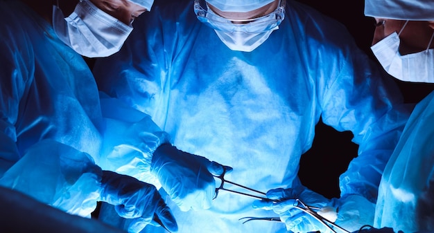 Group of surgeons wearing safety masks performing operation. Medicine concept.