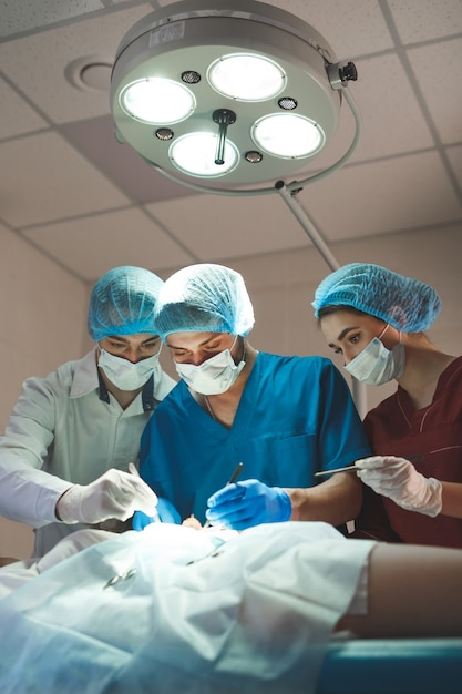 Group of surgeons at work operating in surgical theatre. Resuscitation medicine team wearing protective masks holding steel medical tools saving patient. Surgery and emergency .