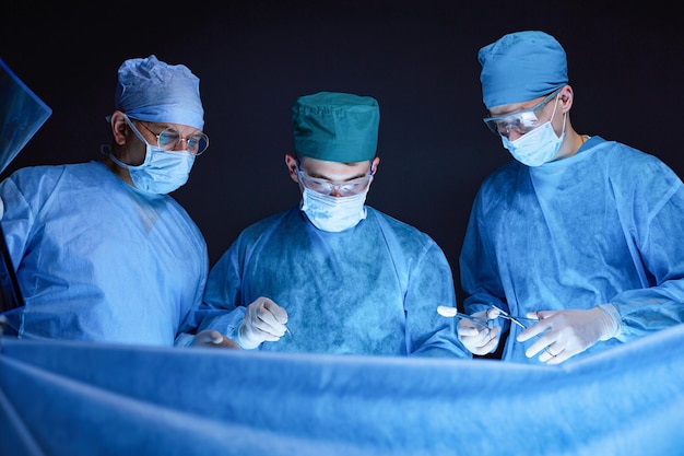 Group of surgeons at work in operating theater toned in blue Medical team performing operation