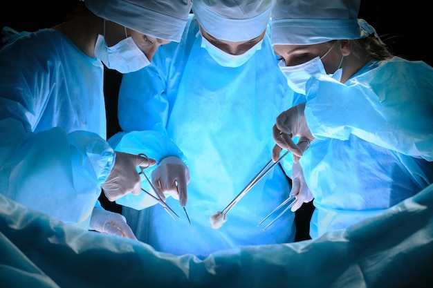 Group of surgeons at work in operating theater toned in blue. Medical team performing operation