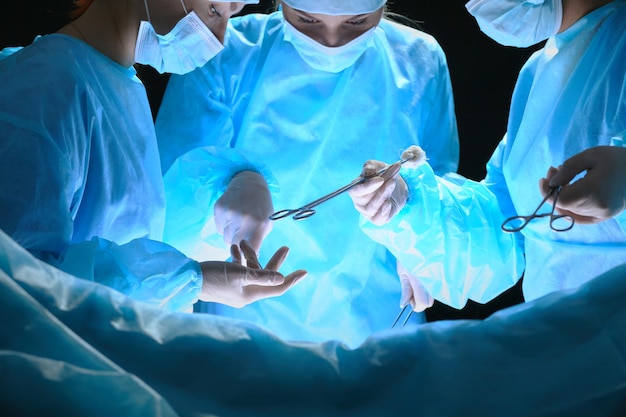 Group of surgeons at work in operating theater toned in blue. Medical team performing operation