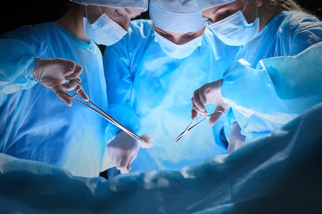 Group of surgeons at work in operating theater toned in blue. Medical team performing operation