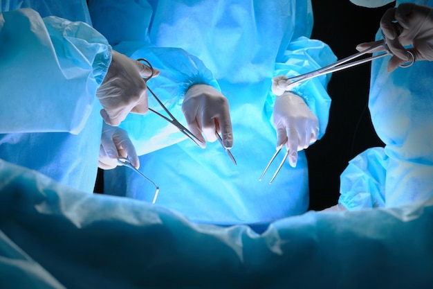 Group of surgeons at work in operating theater toned in blue. Medical team performing operation