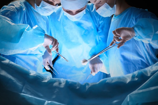 Group of surgeons at work in operating theater toned in blue. Medical team performing operation