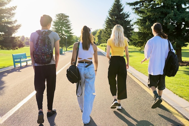 Group of teenage friends on sunny summer day walking together on road back view