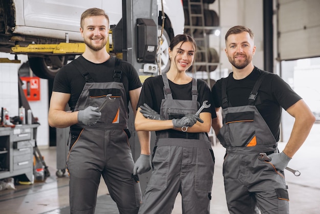 Photo group of three car service technician men and woman talking at workplace people working together at vehicle repair garage service shop check and repair customer car at automobile service center