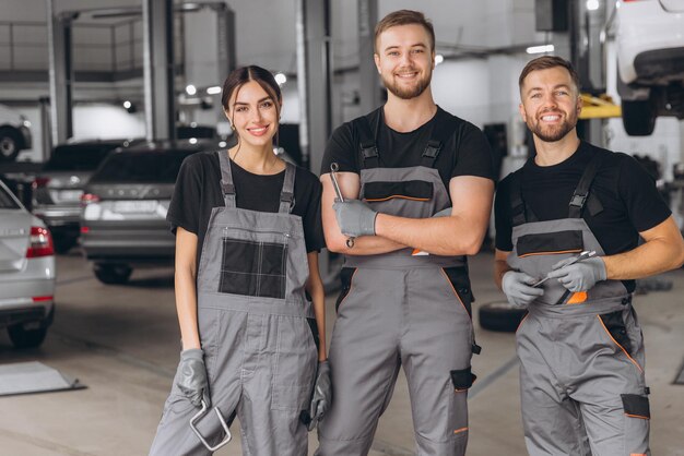 Photo group of three car service technician men and woman talking at workplace people working together at vehicle repair garage service shop check and repair customer car at automobile service center