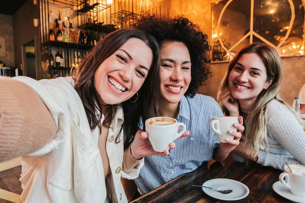 Group of three happy young women taking a selfie portrait on a coffee shop Multi ethnic friends taking a photo smiling and looking at camera