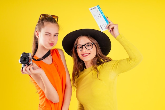 group of three laughing girls holding passports and tickets with photo camera wrapped in american flag spring party summer style yellow background studio, visa and independence day usa