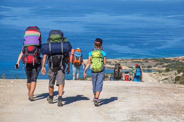 A group of tourists with large backpacks walk along a dirt road overlooking the Mediterranean Sea Cyprus island