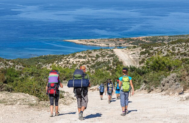 A group of tourists with large backpacks walk along a dirt road overlooking the Mediterranean Sea Cyprus island