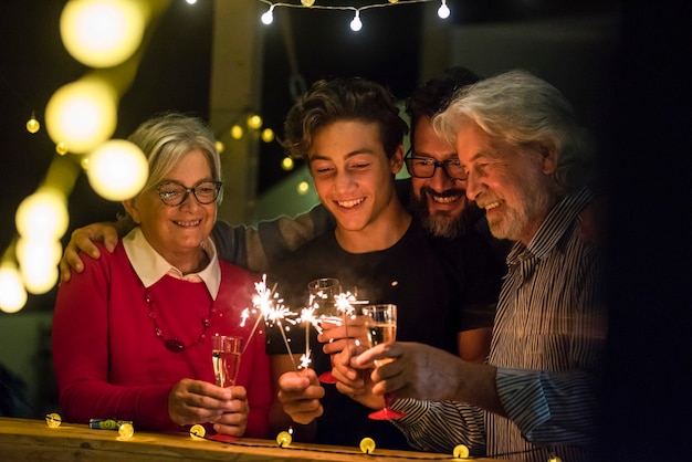 Group of two seniors and an adult and a teenager together having fun with sparlers the new year to celebrate - happy family with lights