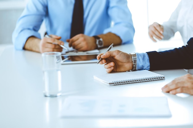 Group of unknown business people discussing questions at meeting in modern office, close-up of hands. Managers at negotiation or brainstorm. Teamwork, partnership and business concept.