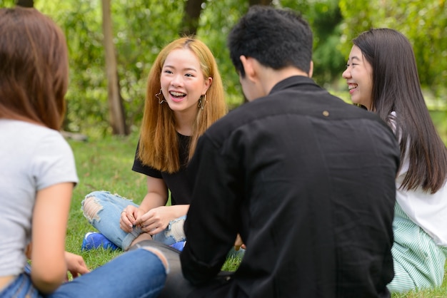 Group of young Asian friends hanging out and relaxing together at the park outdoors