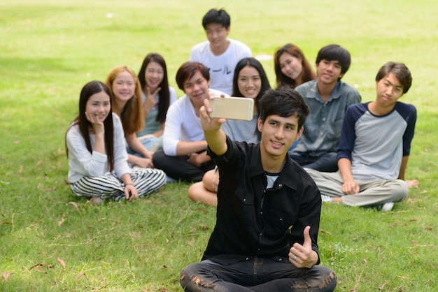 Group of young Asian friends hanging out and relaxing together at the park outdoors