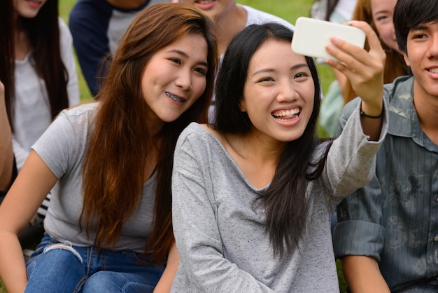 Group of young Asian friends hanging out and relaxing together at the park outdoors