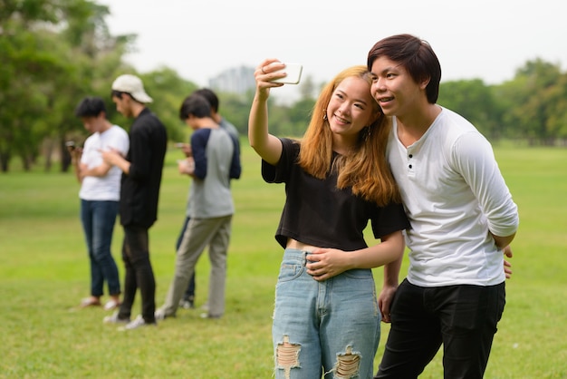 Group of young Asian friends hanging out and relaxing together at the park outdoors