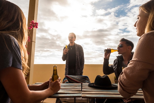 group of young caucasian people stay together in the rooftop terrace speaking and drinking beers