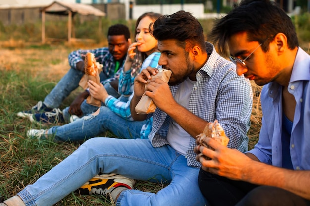 The group of young diverse people eating fastfood on nature